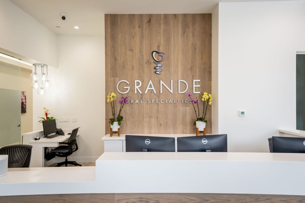 Modern dental office reception area featuring white front desk, wood accent wall with 
