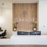 Modern dental office reception area featuring white front desk, wood accent wall with 