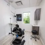 Treatment operatory with dental chair, wall-mounted equipment, window for natural light, and clean modern design with light-colored finishes